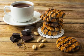 Chocolate icing cookies with peanuts and cup of tea on a rustic wooden table. Breakfast biscuits and tea.
