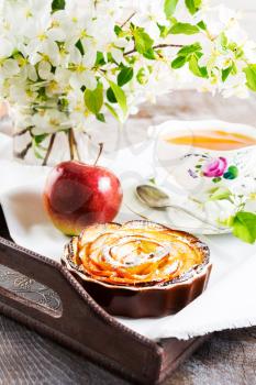 Apple rose shaped pie and cup of tea on the vintage serving tray. Breakfast tea with sweet apple pastry. Homemade apple cake for tea time.