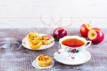 Cup of tea and apple roses shaped muffins on rustic wooden table. Sweet apple dessert pie. Homemade apple rose pastry. Breakfast tea with sweet apple pastry