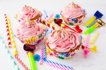 Birthday party concept with pink cupcakes. Colored striped drinking straws, birthday party candles and cupcakes with whipped cream. Birthday invitation background.