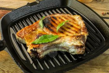 grilled meat on a grill pan with green laurel leaves wooden background