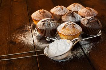 Vanilla and chocolate muffins, caster sugar, sieve for a baking on a dark wooden background, selective focus