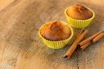Muffins in the yellow paper cupcake holder on sackcloth and cinnamon sticks, selective focus