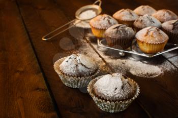 Muffins, caster sugar, sieve for a baking on a dark wooden background, selective focus