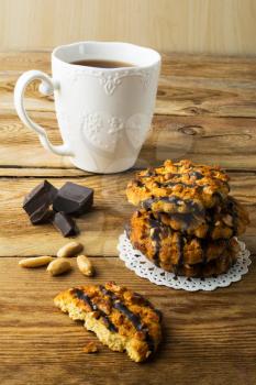 Chocolate icing cookies with peanuts and tea on a rustic wooden table, vertical. Breakfast biscuits and tea.