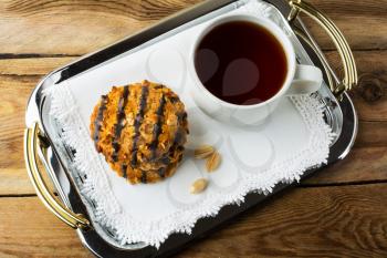 Peanut cookies coating chocolate and a cup of tea on a metal serving tray with handles covered with a white lace napkin, top view. Breakfast biscuits and tea.
