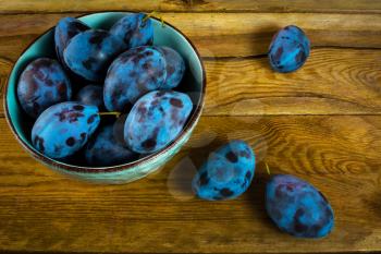 Fruit plums prunes in turquoise cup on the old dark wooden background top view. Selective focus