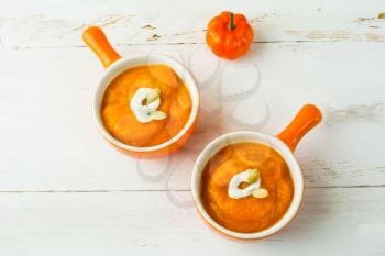 Pumpkin squash vegetable soup with cream in a cocottes, orange serving plate with handle, top view