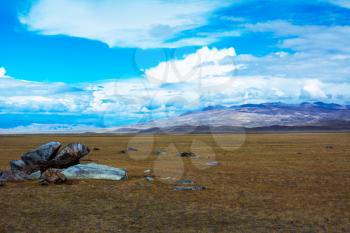 Steppe landscape with a piece of rock in the foreground, mountains view, blue sky with clouds. Chuya Steppe,  Kuray steppe in the Siberian Altai Mountains, Russia