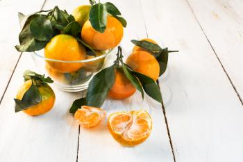 Ripe tangerines with green leaves in a glass bowl on a white wooden background horizontal