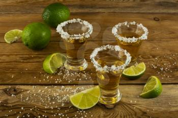 Three tequila shots with lime and salt on the wooden background. Gold Mexican tequila. Tequila shot. Tequila