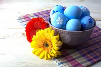 Blue Easter eggs in a purple bowl and flower on a white wooden background. Easter background. Easter eggs. Easter. Easter hunt. Easter symbol.  Easter card. Easter greetings. Happy Easter