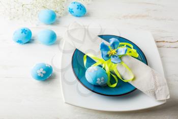 Blue Easter table place setting with plate, napkin and Blue Decorated Easter eggs on white wooden background