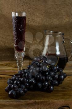 Bunch of dark grapes and a glass of wine on a dark wooden background. Bunch of grapes. Cluster grapes.  Bunch grapes. Grapes. Grape. Glass of wine. Glass wine. Grape vine