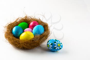 Multicolored Easter eggs in a nest and blue Easter egg with floral design on white background. Easter background. Easter symbol. Copy space