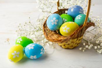 Hand-painted decorated Easter eggs in the basket with small white baby's breath flowers on a white wooden background, close up
