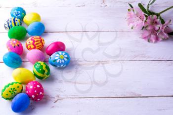 Multicolored hand-painted Easter eggs and pink flowers on white wood plank. Easter background. Easter symbol. Top view with copy space