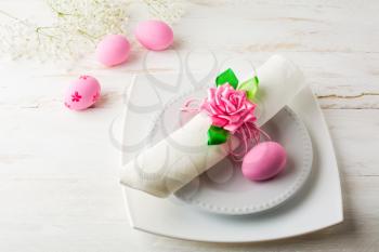 Pink Easter table place setting with plate, napkin and Pink Decorated Easter eggs on white wooden background, top view