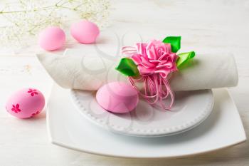 Pink Easter table place setting with plate, napkin and Pink Decorated Easter eggs on white wooden background 