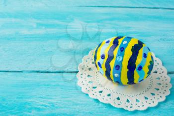Нand-painted yellow Easter egg with abstract design on a blue wood plank background. Easter background. Easter symbol. Copy space