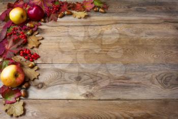 Border of apples, acorns, berries and fall leaves on the old wooden background. Thanksgiving background with seasonal berries and fruits. Abundant harvest concept.