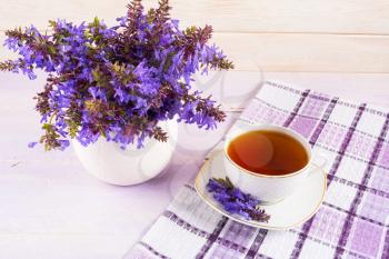 Cup of tea on checkered napkin and purple flowers. Summer tea time concept. Breakfast tea cup served with flowers.
