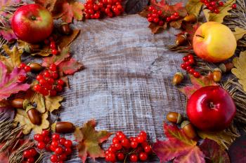 Frame of apples, acorns, berries and fall leaves on the rustic wooden background. Thanksgiving background with seasonal berries and fruits.  