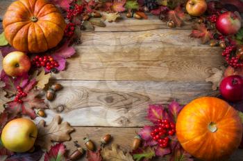 Frame of pumpkins, apples, acorns, berries and fall leaves on wooden background. Thanksgiving background with seasonal vegetables and fruits.  