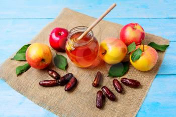 Glass honey jar, dates and apples on burlap napkin. Jewesh new year symbols. Rosh hashanah concept. Organic fruits.