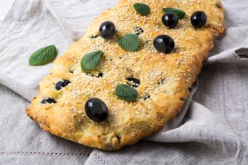 Italian bread focaccia with olive, garlic and herbs on the linen napkin. Homemade traditional Italian bread focaccia.