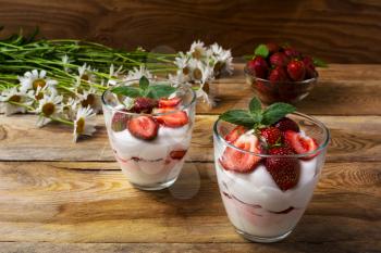 Layered strawberry yogurt dessert on wooden background. Diet yogurt dessert with ripe strawberry