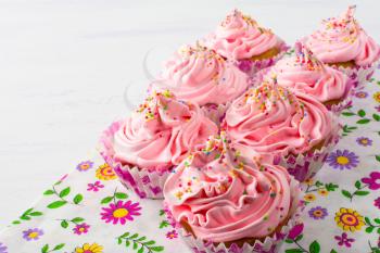Pink cupcakes  on floral napkin. Birthday cupcake with whipped cream. Homemade cupcakes served for party. Birthday background.