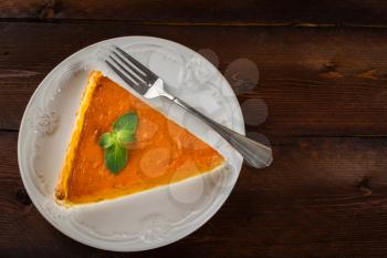 A piece of pumpkin pie with mint, white plate, fork on dark wooden background, copyspace