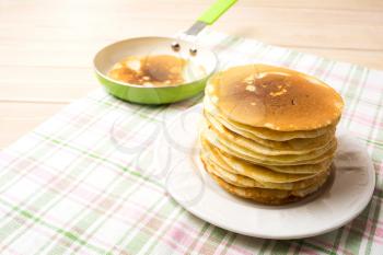 Stack of breakfast pancakes on the white plate and green pan. Homemade pancakes served for breakfast.