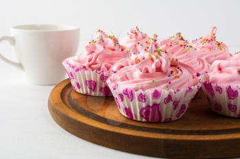Tea time with pink cupcakes.  Birthday cupcake with whipped cream and cup of tea. Homemade cupcakes served on wooden board. 