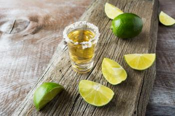 Tequila shot with lime slices on rustic wooden background. Strong alcohol  drink. Gold Mexican tequila shot. 