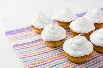 White birthday cupcakes on the striped  linen napkin. Homemade cupcakes with whipped cream.  Birthday party cupcakes. 
