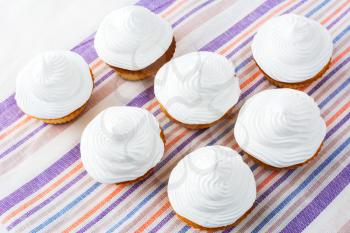 White cupcakes on the striped linen napkin top view. Sweet gourmet pastry dessert. Homemade cupcakes with whipped cream.  