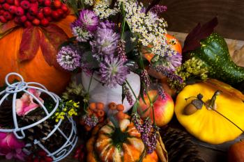 Thanksgiving arrangement with yellow, green, orange squash, white birdcage, cones, apples and purple clower flowers