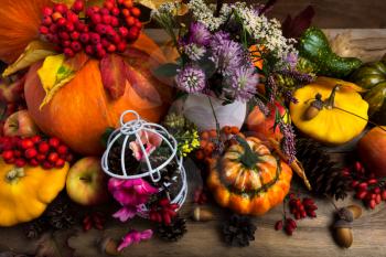Thanksgiving arrangement with orange pumprin, yellow, green, turban squash, white birdcage, cones, apples and purple clower flowers, top view