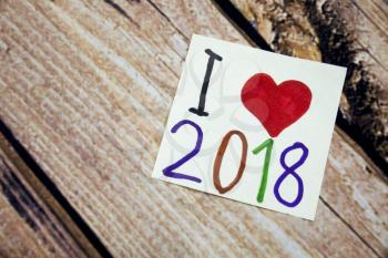 I love 2018 year with red heart symbol. Handwritten message on the white paper with wooden bark in the background. Positive concept with 2018 number on the paper.