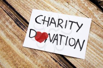 Conceptual image with Charity Donations handwritten message on the white paper with wooden background. Health and god will concept and with red heart. Help for people having no money.