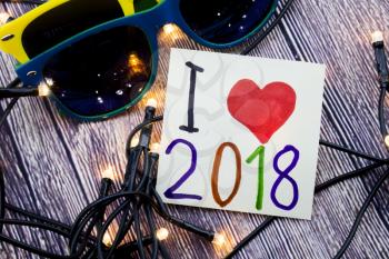 I love 2018 love concept on paper. small designing lights are provided in various order. Glasses of various colors with wooden background. Concept either in some business or in relationship.