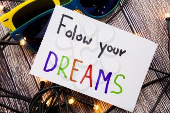 Follow your dreams motivational handwritten message on paper above retro wooden background with lights spread in distinctive ways. Picture represents motivation with positive words.