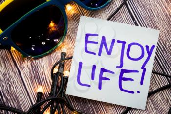 Enjoy life motivational handwritten message on paper with blue color on wooden background with lights spread in unmistakable headings. Motivational concept like lifestyle for people.