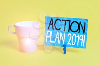 Handwriting text Action Plan 2019. Conceptual photo proposed strategy or course of actions for current year Cup empty paper blue clothespin rectangle shaped reminder yellow office