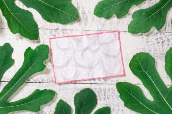 Leaves surrounding notepaper above a classic wooden table as the background