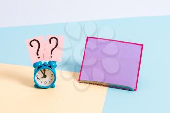 Mini size alarm clock beside a Paper sheet placed tilted on pastel backdrop