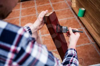 Painted wooden board with painting brush. Home renovation and DIY concept. Young man holding the brushes. painter doing table leg with brown color