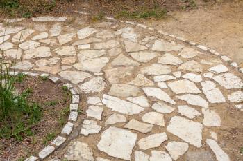 Block of stones forming a circular pathway. Patterned bricks lining the pavement. Unwanted weeds growing in the soil.Non conventional backyard and garden design